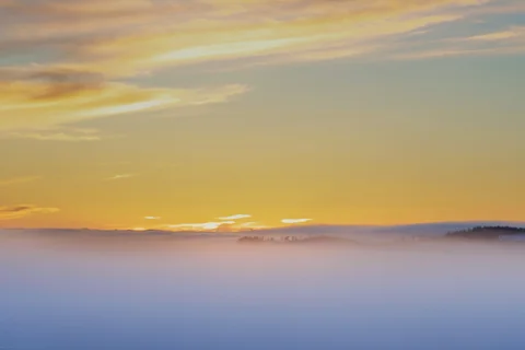A low blanket of mist beneath a golden sky, with a dark horizon in the distance.